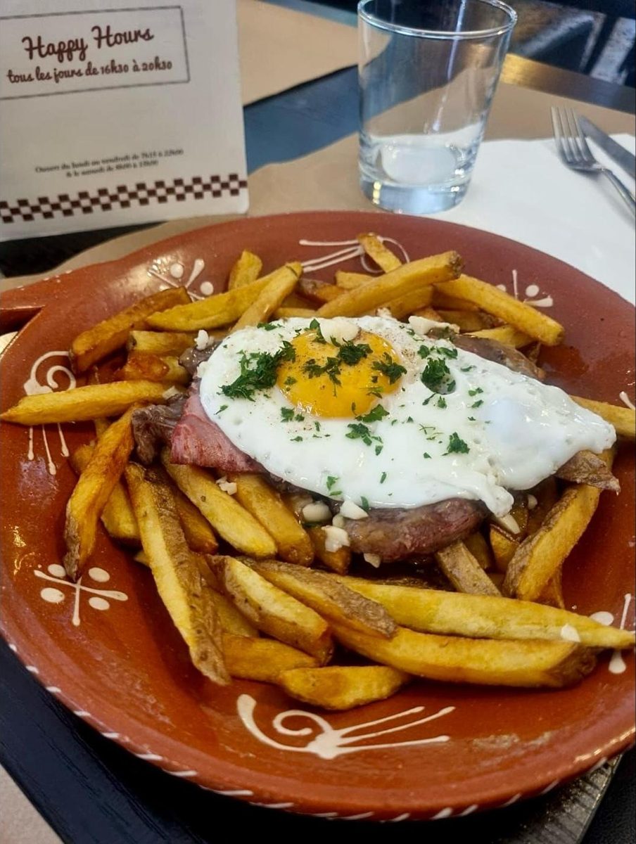 Viande, frites maison et œuf au plat dans un plat en terre cuite